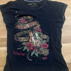 Svart t-shirt från Hard Rock Cafe - Cool svart t-shirt från Hard Rock Cafe med tryck av en gitarr och röda rosor. möts bara upp!