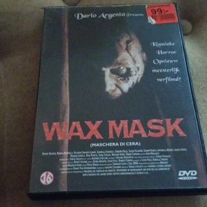 Wax Mask DVD - DVD-film 'Wax Mask' presenterad av Dario Argento. Omslaget har en skräckinjagande bild av en vaxmask och texten 'Klassieke Horror Opnieuw meesterlijk verfilmd!'.