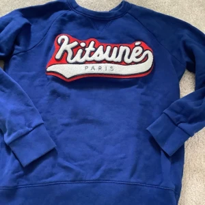 Blå tröja från Maison Kitsuné - Säljer en snygg blå tröja från Maison Kitsuné med ett stort, coolt tryck på framsidan. Tröjan är gjord av 100% bomull och är superbekväm. Perfekt för både höst och vår! 🌀Storlek S men passar som xs