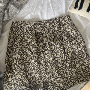 Blommig kjol från GAP - Säljer en superfin blommig kjol från GAP. Den är kort och perfekt för både vardag och fest. Kjolen har ett svart och beige mönster som ger en stilren look. Materialet känns bekvämt och passar bra till olika tillfällen. Perfekt att matcha med en enkel topp eller en stickad tröja!