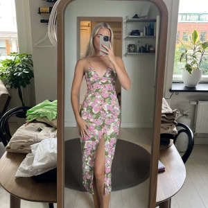 Blommig klänning med slits - Säljer en superfin blommig klänning med smala axelband och en snygg slits framtill. Klänningen har en öppen rygg med snörning, vilket ger en extra touch. 