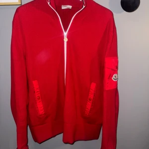 Röd tröja med dragkedja från Moncler - Säljer en snygg röd tröja från Moncler med dragkedja och coola detaljer. Den har en ficka med Moncler-logga på ärmen och ribbade muddar. Perfekt för att hålla stilen i höst och vinter! Orsaken till försäljning är att jag inte har använt den som jag hade tänkt mig, använd fåtal gånger och känner att den kan komma till nytta hos någon annan. Riktigt fet tröja och den är inte jätte vanlig då jag inte har sett någon med liknande innan, o de gör den lite fetare. Ny pris 7999kr (Mitt pris 5500kr)