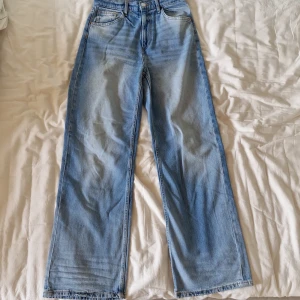 Blå jeans med normalhög midja från H&M - Säljer ett par snygga blå jeans från H&M. De har en hög och justerbar midja för perfekt passform. Byxorna har en wide leg-stil. De är i bra skick och har en dragkedja och knapp framtill. Använda typ en gång därav priset. Nypris 279kr