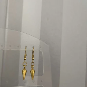 Guldiga konformade örhängen - Säljer ett par snygga guldiga örhängen med en cool konformad design. Perfekta för att ge lite edge till din outfit! De är i nyskick och redo att bäras till både vardag och fest.