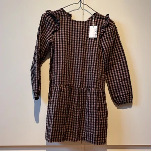 Rutig klänning - Brun/svart rutig klänning i storlek 140 från Pieces. Nya, aldrig använd. Ordinarie pris 350 kr.