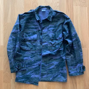 Camouflage jacka/fieldjacket - Vintage blå camouflage fieldjacka. Köpt i Paris. Skick 9/10. Storlek small. Den har en färgfläck på vänster underärm (visas i annons). Supersnygg och passar till allt, perfekt till hösten. 