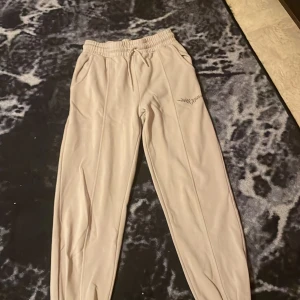 Beige mjukisbyxor med tribaltryck - Säljer ett par bekväma beige mjukisbyxor med ett coolt tribaltryck på sidan. Byxorna har elastisk midja med snörning och två fickor fram. Perfekta för en avslappnad dag hemma eller en snabb tur till affären.