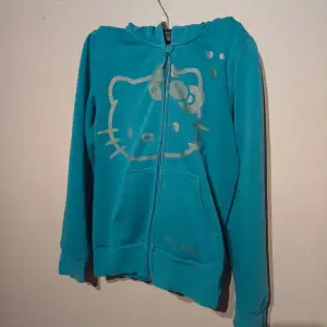 Säljer en superfin turkos hoodie med Hello Kitty-motiv i silver. Den har en dragkedja framtill och är perfekt för en avslappnad stil. Passar både till vardags och mysiga hemmakvällar. 🐱✨ står ingen strl men passar xs/s