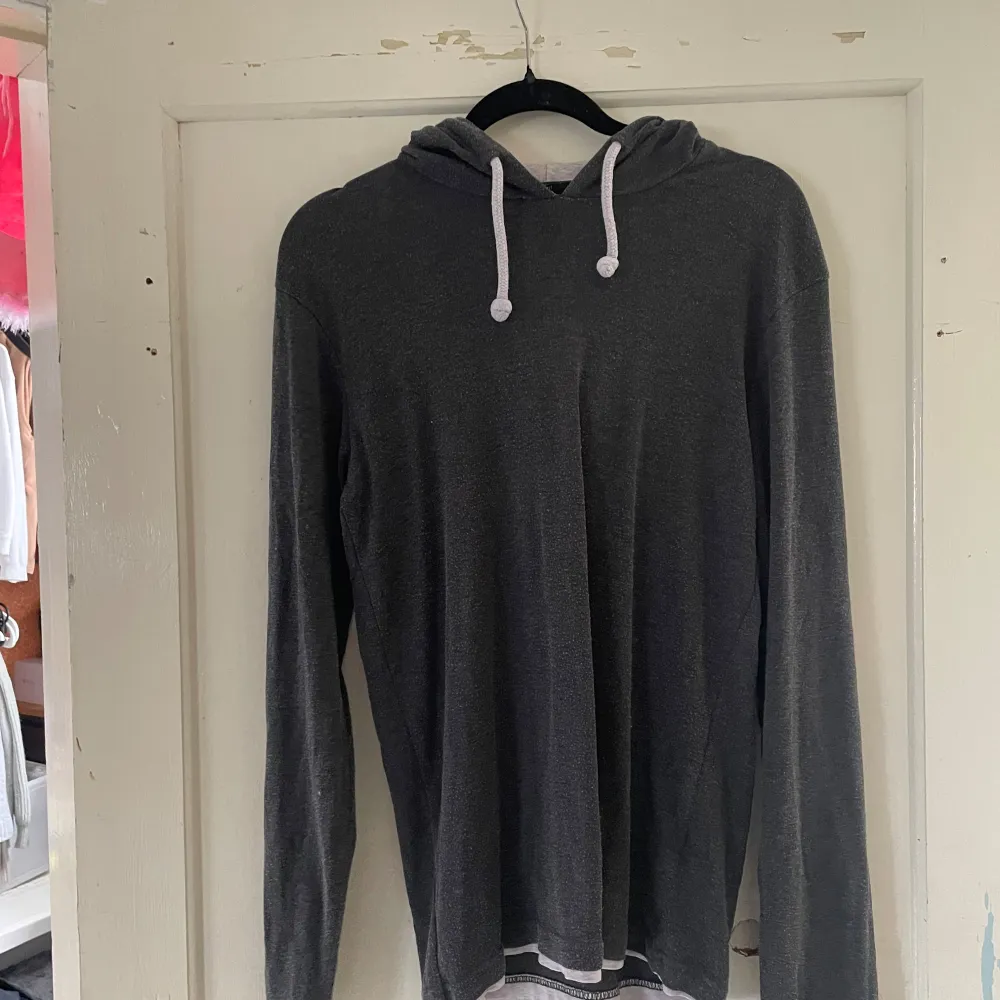 Säljer en stilren grå hoodie i slim fit. Den har en mjuk och bekväm känsla med vita dragsnören i huvan. Perfekt för en avslappnad look under höst och vinter. Passar bra till både jeans och joggers!. Tröjor & Koftor.