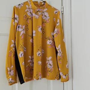 Gul blommig blus - Säljer en superfin gul blus med blommigt mönster i rosa och vitt från Soaked in luxury. Blusen har långa ärmar och knappar vid ärmsluten som ger en söt detalj. Perfekt för både vardag och fest!
