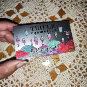 Praline Palette från Trifle Cosmetics - Säljer en superfin ögonskuggspalett från Trifle Cosmetics som heter Praline Palette. Den har sex olika nyanser som är perfekta för både vardag och fest. Färgerna inkluderar en djup lila, skimrande grå, mörkbrun, rödbrun, olivgrön och en varm koppar. Paletten är vegansk och cruelty-free, vilket är ett stort plus! Den är också fri från mineralolja, parabener och gluten. Perfekt för dig som vill ha en mångsidig och etisk sminkprodukt.