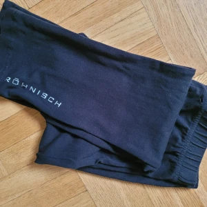 Träningstights Svarta 150/160 tjej - Svarta tights Röhnish Girl Power m silverlogga nertill på ena benet. Stl 150/160 Mått: ca 63cm i midja runt om, längd ca72cm. Bomull, elastan.