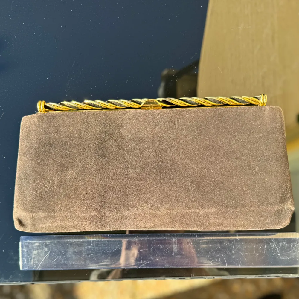 Svart kuvertväska / clutch. Väskan har guldfärgad ram och en vriden gulddetalj upptill. Insidan är fodrad med ett fack med dragkedja. Perfekt för en kväll ute eller en speciell tillställning! Mått -se linjal. Hämtas på Hägerstensåsen eller ök 🖤. Laukut & Käsilaukut.