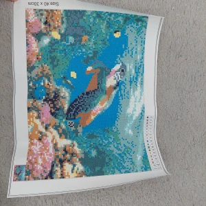 Diamanttavla med fågelmotiv - En färgglad diamantmålning med ett fågelmotiv. Storleken är 40 x 30 cm. Tavlan har en blandning av blå, rosa, bruna och gröna nyanser som skapar en levande och detaljerad bild av en sköldpadda i havet.