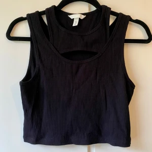 Svart ribbad croppad linnetopp - Snygg svart ribbad linnetopp i croppad modell.  Toppen har en stilren design med breda axelband och ärmlös stil. Passar både till vardags och festliga tillfällen.