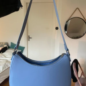 Blå axelväska med dragkedja - Säljer en superfin blå axelväska i syntetmaterial. Den har en stilren design med en praktisk dragkedja upptill. Perfekt för både vardag och fest! 💙Orginalpris 300kr