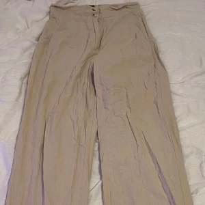 Beige byxor från Emery Rose - Säljer ett par snygga beige byxor från Emery Rose i storlek M. De är högmidjade med en loose passform och har knappar framtill. Perfekta för både vardag och fest! 🥳lätt material säljs för 70