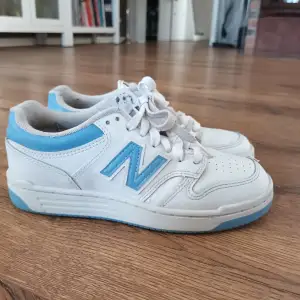 Säljer ett par vita sneakers från New Balance med ljusblå detaljer. Skorna har snörning och är i bra skick med lite slitage. Perfekta för vardagsbruk och ger en sportig look. Använda en sommar 