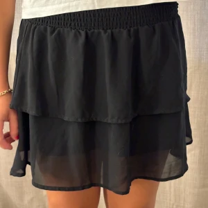 Svart kortkjol med volang - Säljer en superfin svart kortkjol med volangdetaljer. Kjolen har en elastisk midja.