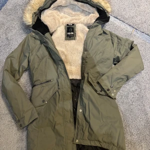Grön parkajacka från 8848 Altitude storlek 36  - Säljer en snygg och varm grön parkajacka från 8848 Altitude. Jackan har en mysig fuskpälsfodrad huva och flera praktiska fickor med dragkedja. Perfekt för kalla vinterdagar! 🧥❄️vind o vattentät. 