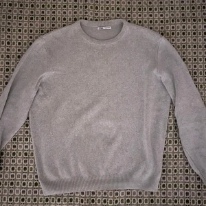 Grå tröja från Zara - Säljer en stilren grå tröja från Zara i storlek M. Perfekt för både vardag och lite finare tillfällen. Tröjan är i mycket bra skick och har en klassisk design med rund hals och ribbade kanter. Supermjuk och bekväm att ha på sig!