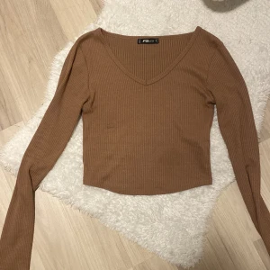 Brun ribbad tröja från FB sisters - Säljer en snygg brun ribbad tröja. Den har en v-ringad hals och långa ärmar, perfekt för höst och vår. Tröjan är croppad och ger en trendig look. Passar både till vardags och fest! 🧡