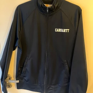 Svart track jacket från Carhartt - Säljer en marin blå track jacket från Carhartt i storlek M. Jackan är i 100% polyester och har en dragkedja framtill. Perfekt för höst och vår med sin stilrena design och bekväma passform. Passar både till vardags och lättare träning.