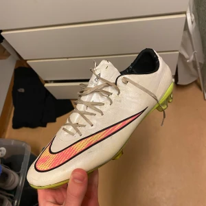 Vita Nike fotbollsskor - Säljer ett par vita Nike fotbollsskor i skick enligt bilder. De har en snygg design med svarta och röda detaljer samt en gul sula. Storlek 43, höger sko är limmad hos skomakare.
