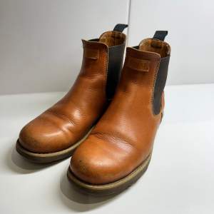 Säljer ett par snygga bruna Chelsea boots från Kavat i skinn, storlek 40. De har en klassisk design med elastiska paneler på sidorna för enkel på- och avtagning. Perfekta för höst och vår, med en robust sula som ger bra grepp. Skorna är i bra skick med lite slitage på tån, men fortfarande superbekväma och stiliga!