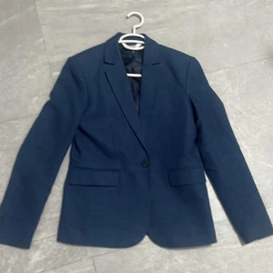 Mörkblå kavaj och byxor - Säljer en stilren mörkblå kavaj med matchande byxor. Perfekt för både fest och formella tillfällen. Kavajen har en klassisk passform med knappar framtill och fickor. Materialet känns bekvämt och passar bra för vår och höst. Ett måste för garderoben!