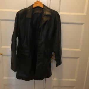 Svart skinnjacka från Leather by Emma - Säljer en svart skinnjacka från Leather by Emma i storlek M. Jackan har en klassisk design med knappar framtill och en stilren krage. Perfekt för höst och vår, och ger en cool look till vilken outfit som helst. Den är i bra skick och redo för nya äventyr!