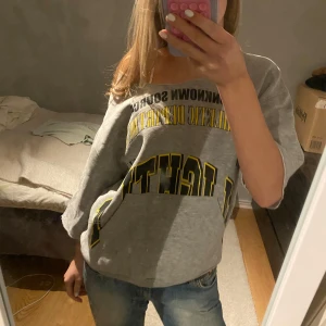 Grå oversized t-shirt med tryck - Säljer en grå oversized t-shirt med tryck i svart och gult. Den har en avslappnad passform och korta ärmar, perfekt för en casual look. Armarna och halsen är avklippta. Perfekt för vardagsbruk eller en chill dag hemma.