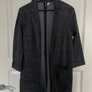Grå kappa med trekvartsärm - Säljer en stilren grå kappa med trekvartsärm. Perfekt för höst och vår, med en klassisk passform och praktiska fickor fram. Materialet är mjukt och bekvämt, vilket gör den idealisk för både vardag och fest. Ett måste i garderoben för den som gillar tidlös stil!