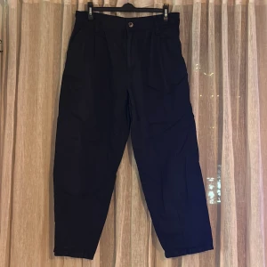 Svarta byxor från 157 - Säljer ett par svarta byxor från märket Lager 157 i storlek L. Byxorna är bylsiga i sin design med knapp och dragkedja framtill. Perfekta för både vardag och festliga tillfällen. De är i mycket bra skick och redo för en ny ägare!