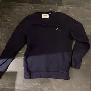 Säljer en snygg mörkblå tröja från Lyle & Scott i mycket bra skick. Den har en broderad gul logga på bröstet och är tillverkad av ekologiskt material. Perfekt för både vardag och lite finare tillfällen. Passar bra till jeans eller chinos!