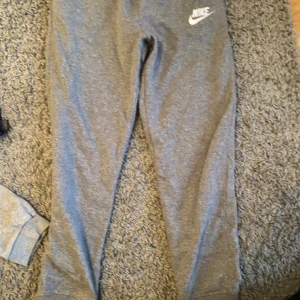 Grå mjukisbyxor från Nike - Säljer ett par grå mjukisbyxor från Nike i bra skick. De är superbekväma och perfekta för chill dagar hemma eller lätt träning. Byxorna har en elastisk midja och muddar vid bensluten för en skön passform. Nike-loggan är snyggt placerad på ena benet. Perfekta för höst och vinter!