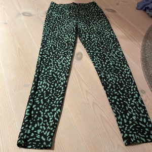 Mönstrade byxor från Lindex - Snygga mönstrade byxor från Lindex i svart och grönt. Perfekta för en cool och avslappnad stil. Tillverkade i Turkiet och i storlek S. Passar bra till både vardag och fest!