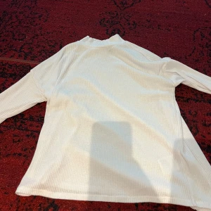 Vit ribbad polotröja - Säljer en stilren vit ribbad polotröja i mycket bra skick. Perfekt för höst och vinter med sin mysiga och varma känsla. Tröjan har långa ärmar och en klassisk polokrage som håller dig varm. Passar både till vardags och lite finare tillfällen.
