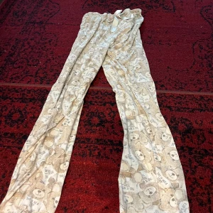 Beige mjukisbyxor med björnmönster - Supermysiga beige mjukisbyxor med gulligt björnmönster. Perfekta för en chill dag hemma eller som pyjamasbyxor. De har en bekväm resår i midjan och är gjorda i mjukt material. Passar perfekt för höst- och vintermys!