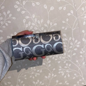 Mönstrad plånbok med dragkedja - Snygg plånbok med ett coolt mönster i svart och silver. Den har flera fack och en praktisk dragkedja inuti för mynt eller småsaker. Perfekt för att hålla ordning på kort och kontanter. Stilren och passar till alla tillfällen!