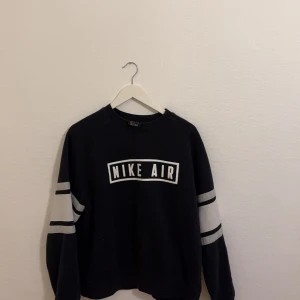 Nike tröja - Säljer en svart Nike Air sweatshirt med vita detaljer och text på bröstet. Tröjan har långa ärmar med vita ränder och en klassisk rund halsringning. Perfekt för en sportig look eller avslappnad stil. (Är som en M)