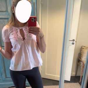 Rosa blus med spetsdetaljer - Söt rosa blus med korta ärmar och spetsdetaljer vid halsringningen. Blusen har en liten knytning framtill och en luftig passform. Perfekt för en somrig look! Eller bara till vardags! Ifrån Odd Molly!!😍