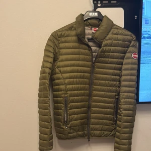 Olivgrön quiltad jacka från Colmar - Säljer en olivgrön quiltad jacka från Colmar. Jackan har en dragkedja framtill och långa ärmar. Den är perfekt för kyligare dagar och har en stilren design med Colmar-logga på ärmen.