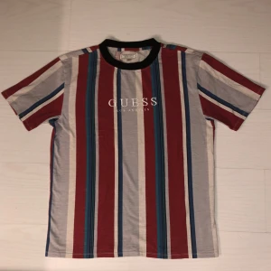T-shirt från Guess - Tandig t-shirt från Guess med ränder i rött, blått och vitt. T-shirten har en klassisk rund halsringning med svart kant och korta ärmar. Vid frågor eller fler bilder kontakta mig. Priset går att diskutera. 