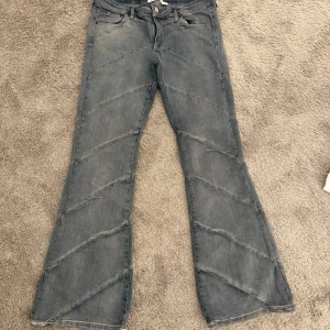 Grå jeans med unikt mönster - Snygga grå jeans med ett diagonalt mönster som ger en cool twist. Byxorna har en bootcut-stil och är perfekta för en avslappnad look. De har klassisk femficksdesign och knappgylf.