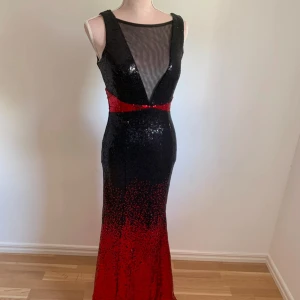 Svart och röd paljettklänning - Snygg långklänning med paljetter i svart och rött. Klänningen har en ärmlös design och en transparent mesh-detalj vid halsen. Perfekt för en glamorös kväll!