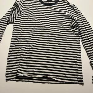 Svartvit randig långärmad tröja - Säljer en stilren svartvit randig långärmad tröja. Perfekt för en avslappnad look. Tröjan har en klassisk rund halsringning och är tillverkad i ett mjukt material för extra komfort.