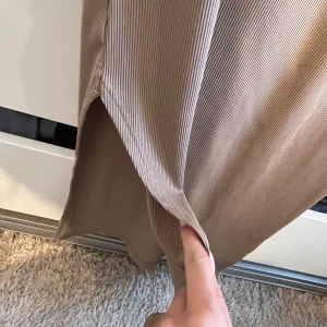 Beige ribbad klänning - Säljer en stilren beige ribbad klänning med korta ärmar och rund halsringning. Perfekt för en avslappnad look. Klänningen har en slits på sidan som ger extra rörelsefrihet.