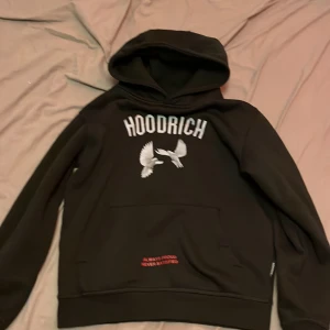 Svart hoodie från Hoodrich - Säljer en svart hoodie från Hoodrich med tryck av vita fåglar och texten 'From Nothing to Something'. Hoodien har en stor ficka framtill och textdetaljer i rött och vitt. Perfekt för en avslappnad stil.