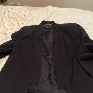 Svart kavaj från Elisabetta Franchi - Elegant svart kavaj från Elisabetta Franchi med stilren design. Kavajen har en diskret gulddetalj och är tillverkad i ett bomullsmaterial. Perfekt för en sofistikerad look.